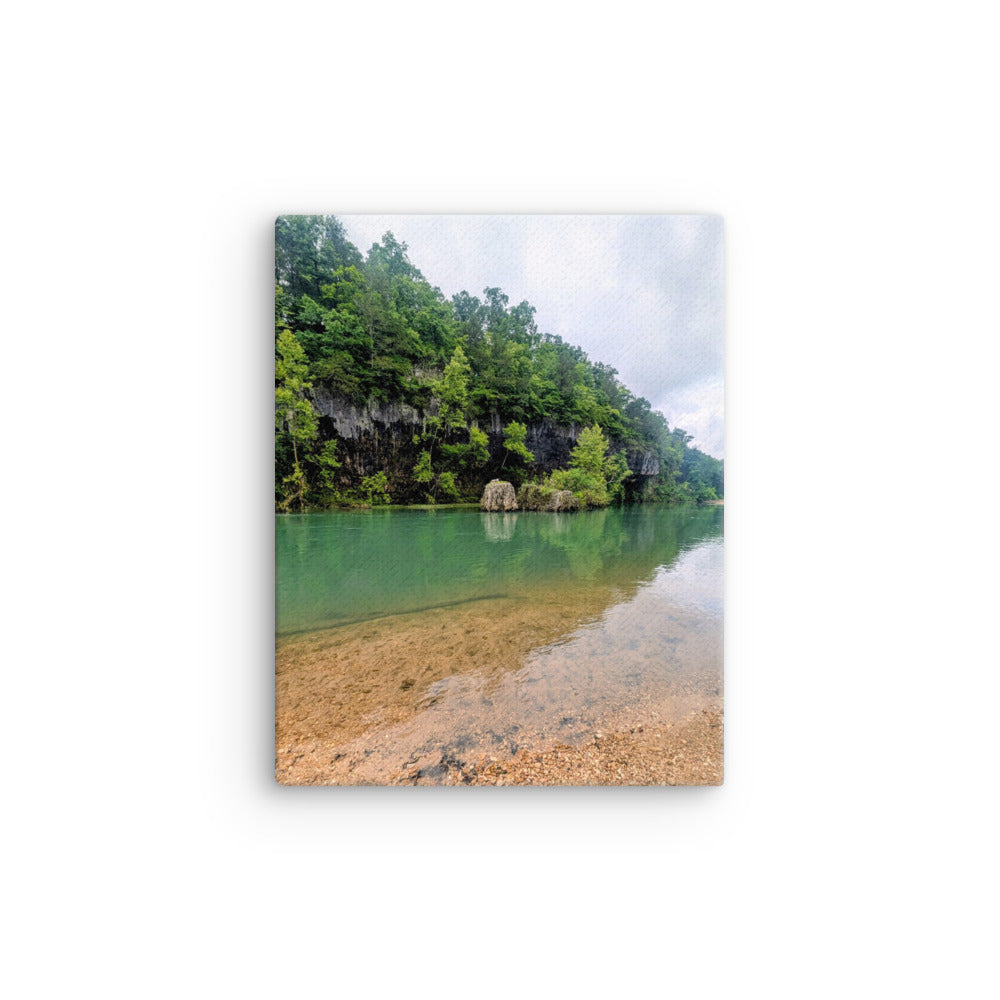 Clear green blue river with rock bluff and forest green with contrasting brown river rock foreground