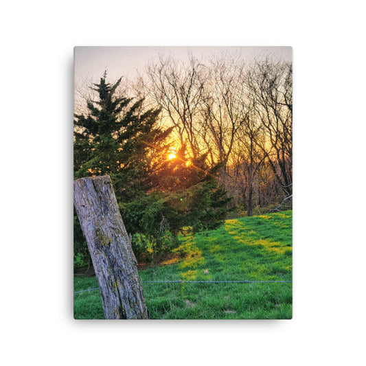 Canvas print of a sunset over a forest with a wooden post in the foreground.