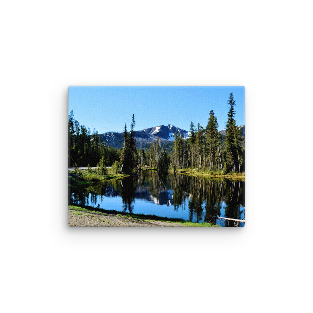 landscape of a reflective lake with evergreen trees and mountain background
