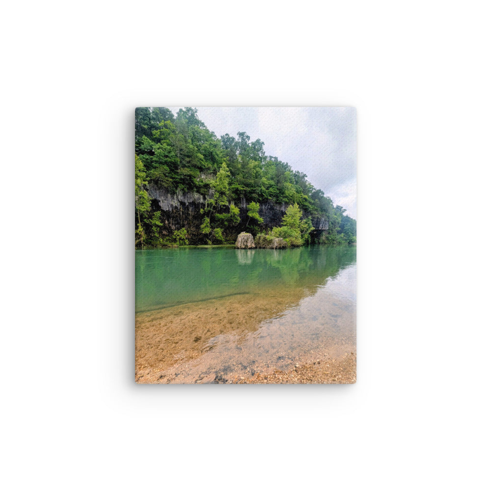 Canvas print of Clear green blue river with rock bluff and forest green with contrasting brown river rock foreground